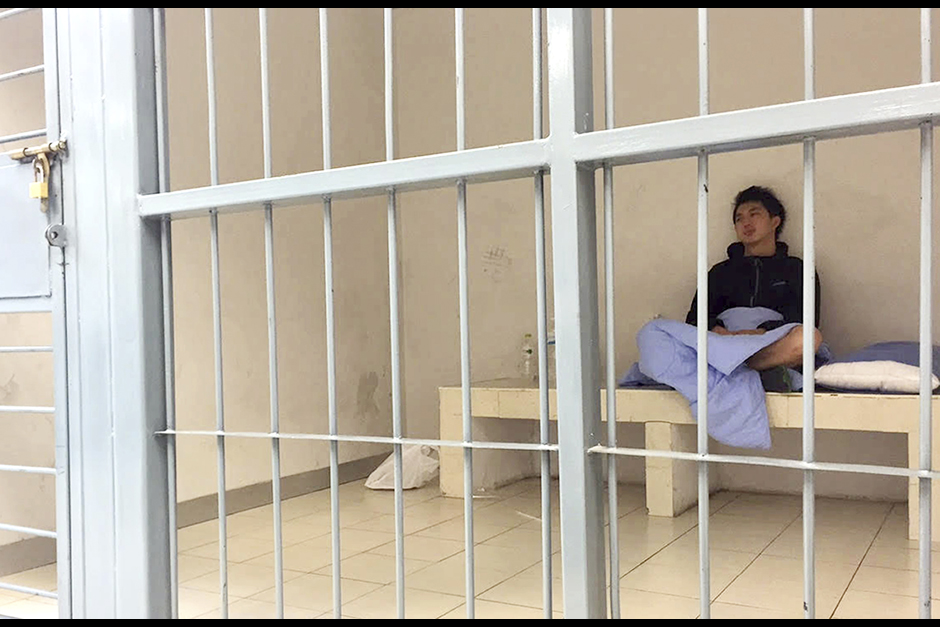 In his image provided by Initium Media Technology, Hong Kong journalist Hok Chun Anthony Kwan sits in a cell, after he was detained at Suvarnabhumi Airport for carrying body armour and a helmet onto a flight bound for Hong Kong. Kwan, who was in Bangkok covering the aftermath of last week's bombing, is being charged with possessing an illegal weapon, which carries a prison sentence of up to five years. - AP