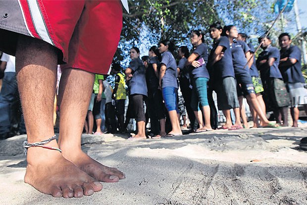 A migrant worker presses his foot into the sand before taking a DNA test, while others queue for similar tests. All male migrant workers on Koh Tao were considered suspects in the murder of two British tourists and required to take footprint and DNA tests. (Photo by Thiti Wannamontha)