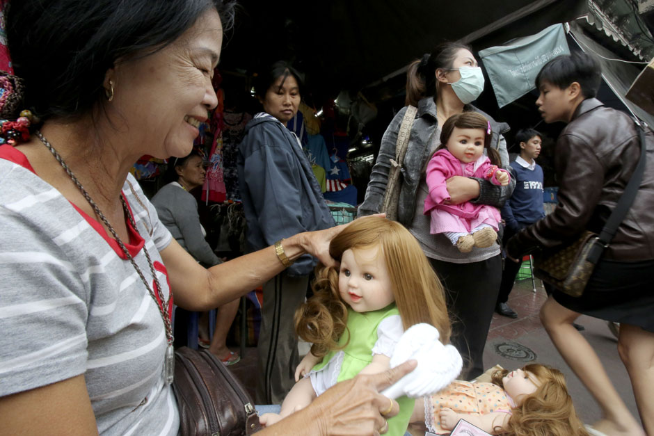 A seller happily combs a Child Angel doll's hair. - Taweechai Tawatpakorn