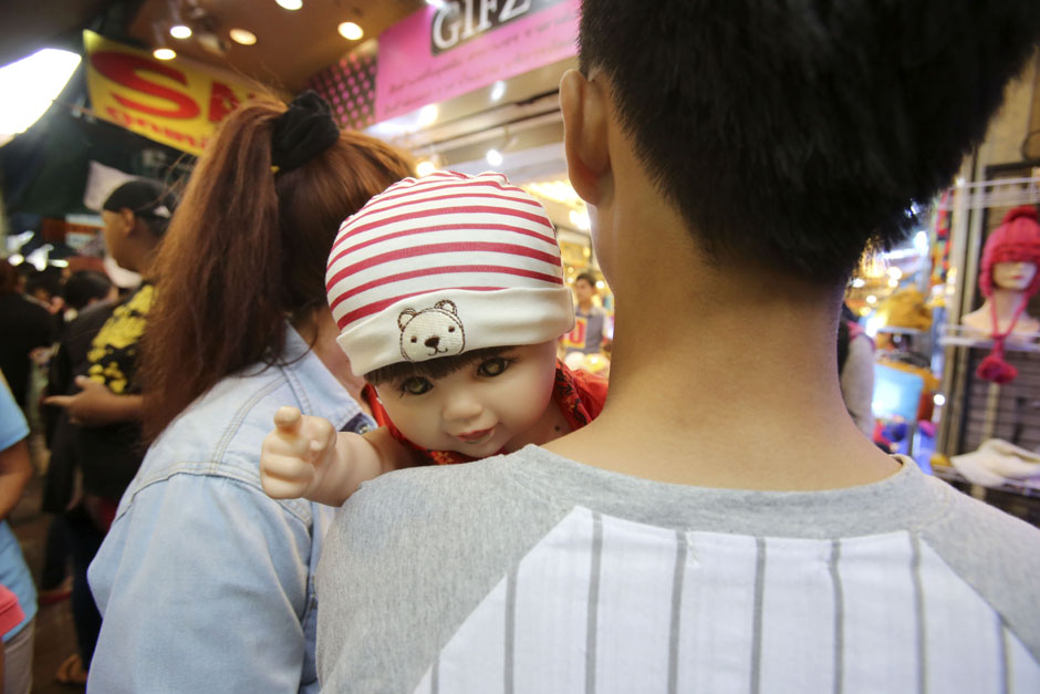 A Child Angel doll points over its owner's shoulder at a market in Bangkok. - Taweechai Tawatpakorn