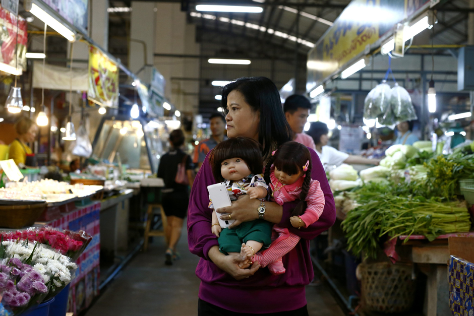 Ms Ratchada holds two of her Child Angel dolls and a smartphone as she shops at a market in Bangkok.