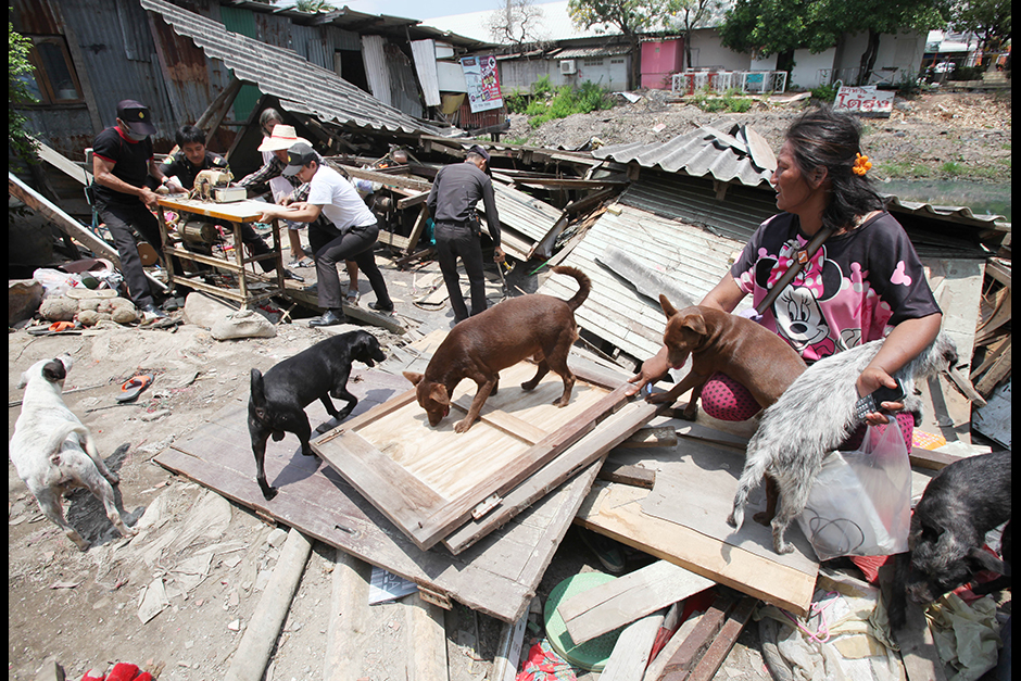 Thanaporn Sangsammon sits by her collapsed home as workers help move her belongings on May 4. Her house in Lam Luk Ka district of Pathum Thani slid into nearby Khlong See after the canal began drying up and the bank subsided. - Apichit Jinakul