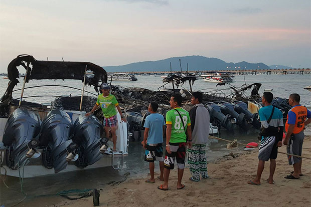 Rescue workers watch over the speed boats damaged by fire at Chalong Beach in Phuket's Muang district early on Tuesday. (Photo by Achadtaya Chuenniran)