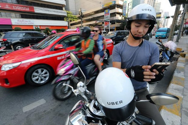 Life in the fast Lane: An UberMoto driver scouts for passengers on his phone while a traditional motosai taxi rides past. (EPA photo)