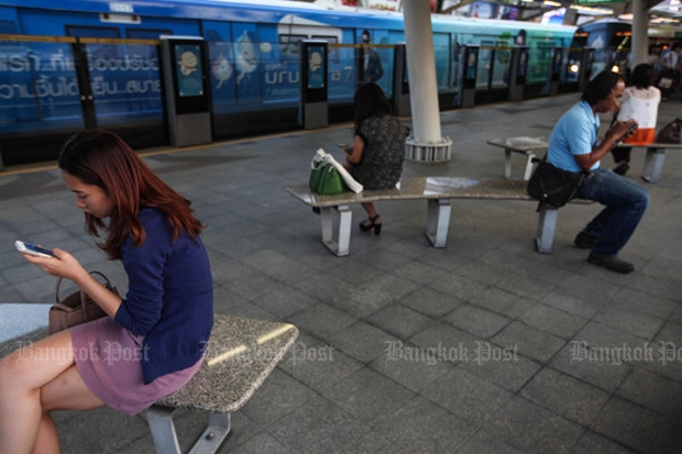 People use their mobile phones while waiting for the train at a BTS station. (Bangkok Post file photo)