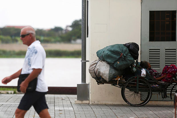 A woman rests on her tricycle as a tourist walks past at the Basac River bank in Phnom Penh on Aug 16, 2016. (Reuters photo)