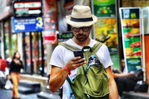 A tourist checks his phone on Silom Road, probably unaware that the National Broadcasting and Telecommunications Commission (NBTC) wants to issue him a special SIM card so he can be closely tracked and monitored. (Photo by Tanaphon Ongarttragoon)