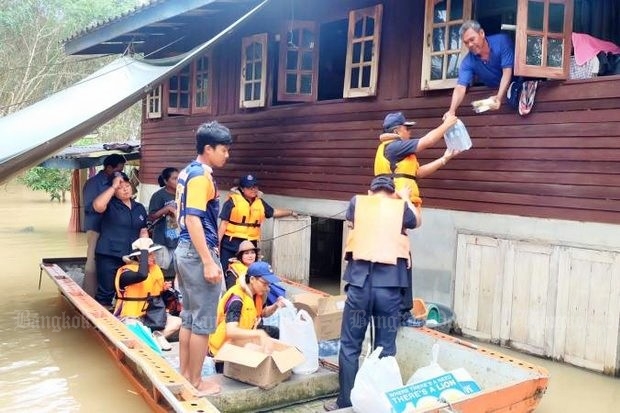 Officials on a flat-bottom boat distribute basic necessities to flood-stranded residents in Surat Thani's Phrasaeng district. (Photo by Supapong Chaolan)