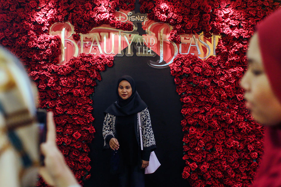 A woman takes a picture of her friend in front of a promotional display for the film 'Beauty and the Beast' in Subang, Malaysia. — EPA