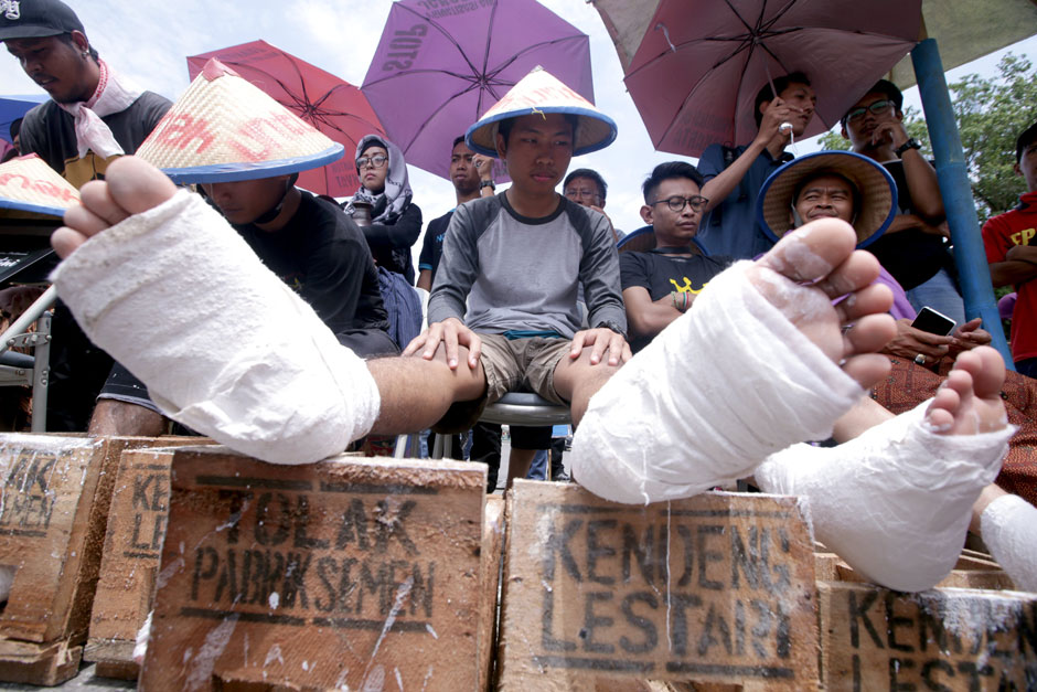 Indonesian activists place their feet, covered in cement, on wooden boxes that read 'Reject cement plan' and 'Conserve Mount Kendeng' during a rally campaign to mark the International Water Day outside the Presidential Palace in Jakarta. They demanded that the government save water and stop the construction of a cement plant in their village in Kendeng Mountain, Central Java. — EPA