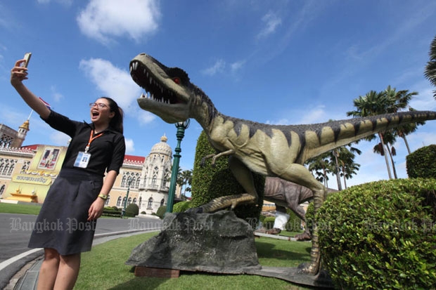 An official at Government House takes a selfie in front of a dinosaur model installed at Government House on Thursday for Children's Day activities this Saturday. (Photo by Thiti Wannamontha)