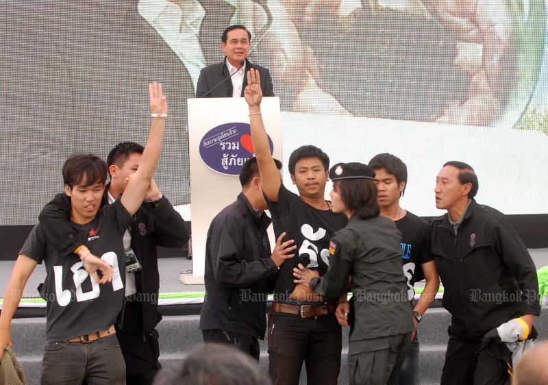 Student activist Jatupat Boonpattararaksa (centre) and other Dao Din members give anti-coup salutes as Gen Prayut Chan-o-cha delivers a speech in Khon Kaen on Nov 19, 2014. (Photo by Chanat Katanyu)