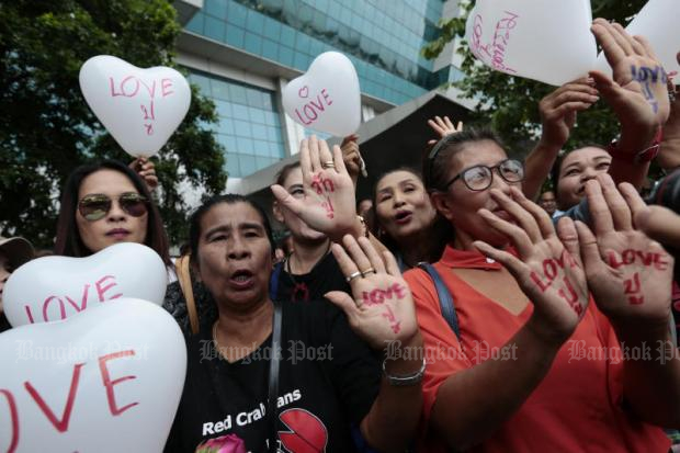 Suppers of former prime minister Yingluck Shinawatra show 'Love Pou" messages written on their palms and on balloons as they offer her moral support on Friday. Pou is her nickname. (Photo by Patipat Janthong)