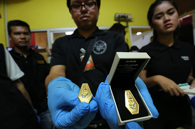 An official shows some of the royal cremation commemorative pins, suspected to be  illegally produced, seized at the  Chayatham Co factory in Bangkok's Lat Phrao district on Friday morning. (Supplied photo)