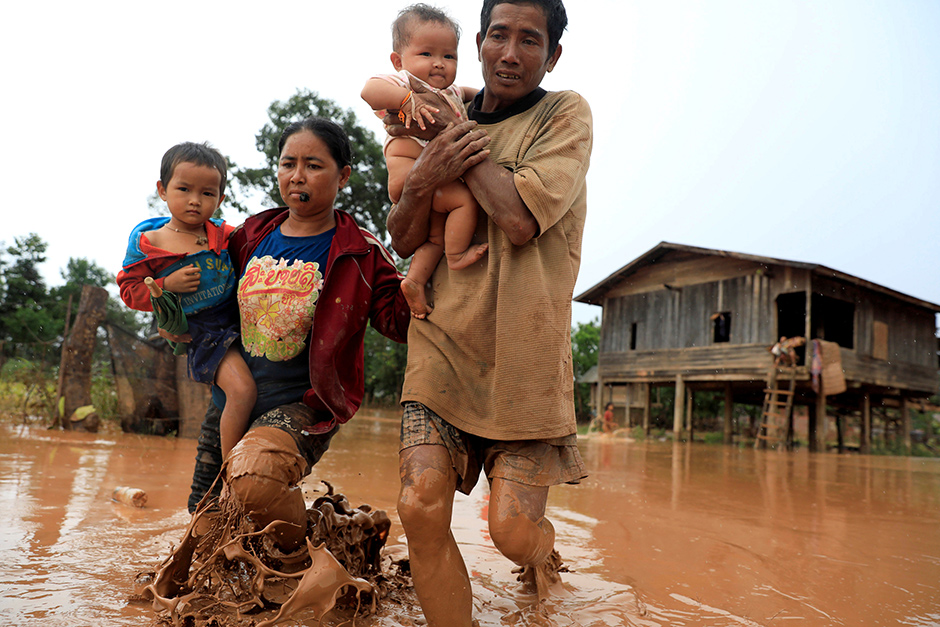 Parents carry their children as they leave their home during the flood on Thursday. — Reuters