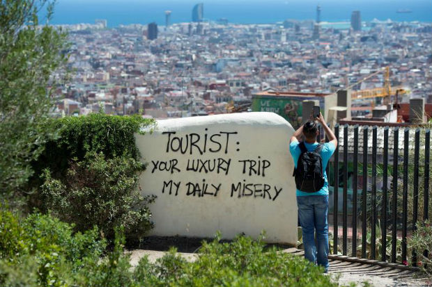 A tourist takes a picture of the city's panorama as he stands next to a wall with a graffiti reading 'Tourist: your luxury trip - my daily misery' on Aug 10, 2017 at Park Guell in Barcelona. (AFP photo) A tourist takes a picture of the city's panorama as he stands next to a wall with a graffiti reading 'Tourist: your luxury trip - my daily misery' on Aug 10, 2017 at Park Guell in Barcelona. (AFP photo)