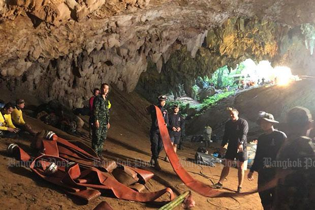 Navy Seal divers and rescuers carry hoses for electric pumps into flooded Tham Luang cave as the search continues for the missing footballers in Chiang Rai province. (Photo by @ThaiSEAL Facebook page)