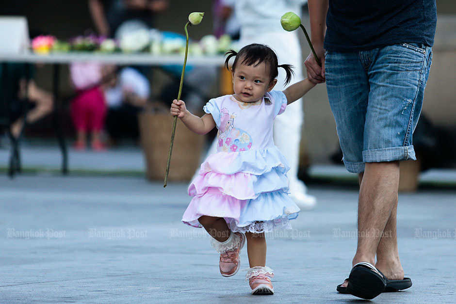 A girl and her father each hold a lotus as they enter Wat Pariwat Ratchasongkhram in Bangkok's Yannawa district. The temple was crowded with Buddhists making merit on Asarnha Bucha Day yesterday. (Photo by Patipat Janthong)