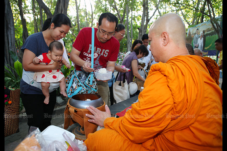 A family offers food to a Buddhist monk at Wat Chonlaprathan Rangsarit in Nonthaburi yesterday. (Photo by Tawatchai Kemgumnerd)