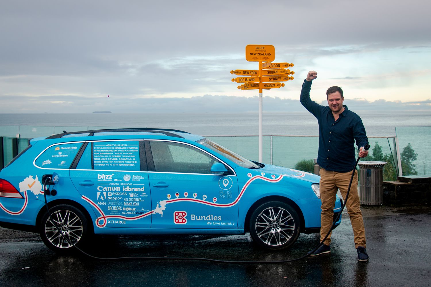 Dutchman Wiebe Wakker holds a charging cable as he poses with his electric vehicle, the Blue Bandit, after travelling 34 countries to reach Bluff, New Zealand's most southern tip, in this handout photo released on Friday. (Wiebe Wakker/Handout via Reuters)