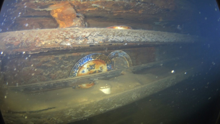 Plates and other artifacts sitting on shelves next to a mess table where a group of lower-ranking crew members would have taken their meals. Plates and other artifacts sitting on shelves next to a mess table where a group of lower-ranking crew members would have taken their meals.