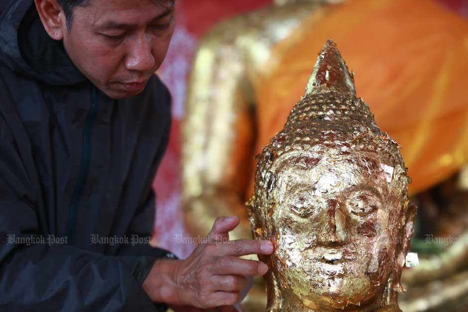 A man places a gold leaf on a Buddha image in a merit-making ceremony on New Year's Eve at Wat Chana Songkhram in Pak Nam district, Samut Prakan. — Somchai Poomlard