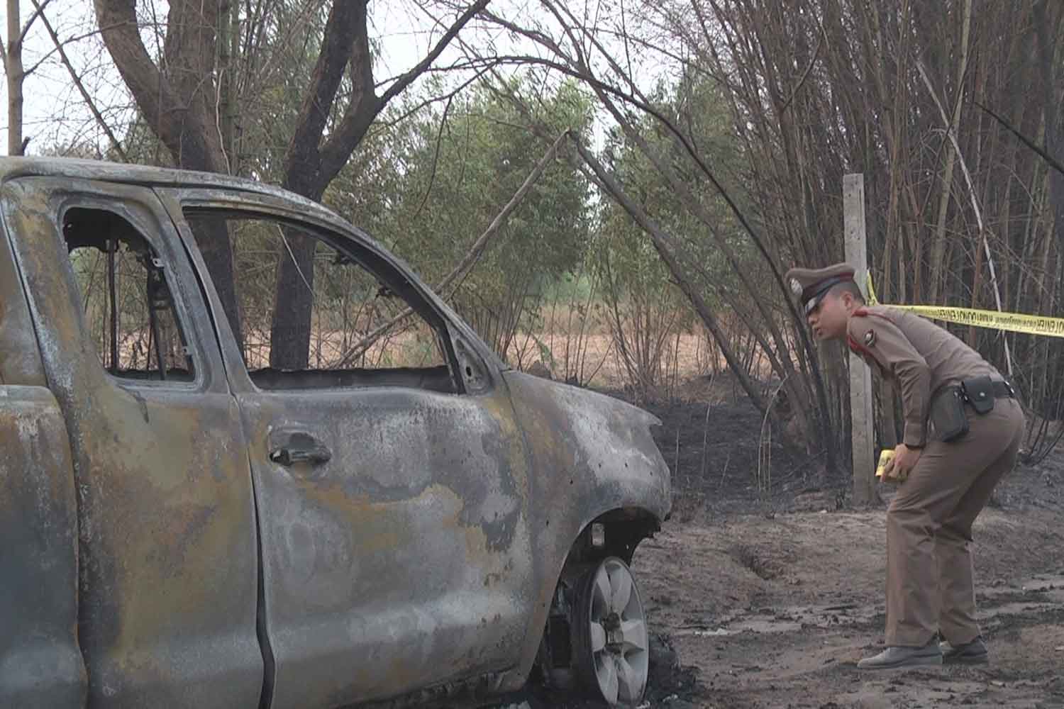A police officer examines the burned-out pickup in which the charred body of a man was found, at a cassava plantation in Muang district of Nakhon Ratchasima on Tuesday. (Photo: Prasit Tangprasert)