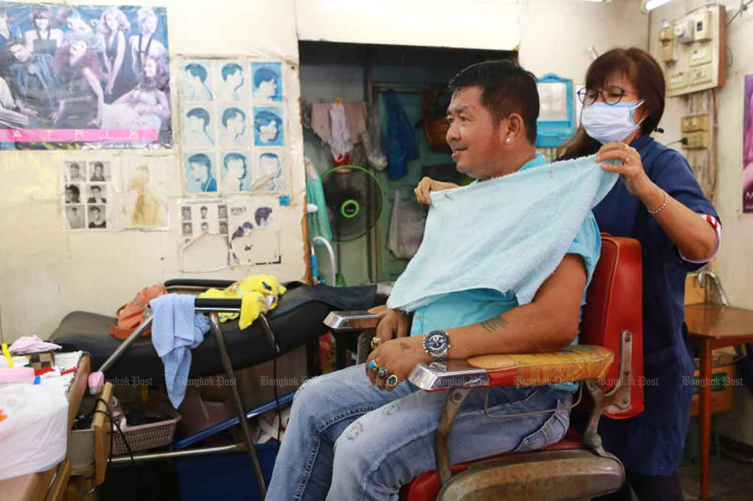 A hairdresser wears a face mask at a shop in Samut Prakan province last month, before the coronavirus shutdown. A decision will be made next week whether barber shops and some other businesses can reopen. (Photo: Somchai Poomlard)