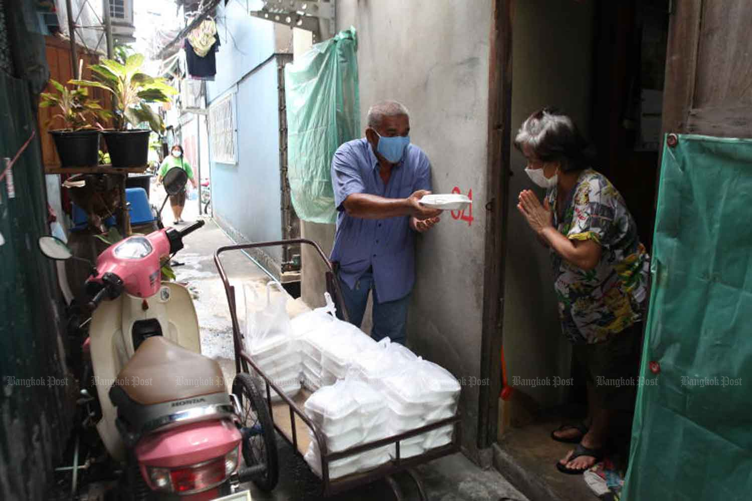 A community leader in Klong Toey district hands out a lunch box to a local resident. The food-sharing project, funded by Muang Thai Insurance Plc, is aimed at helping vulnerable individuals affected by the Covid-19 pandemic. Arnun Chonmahatrakool