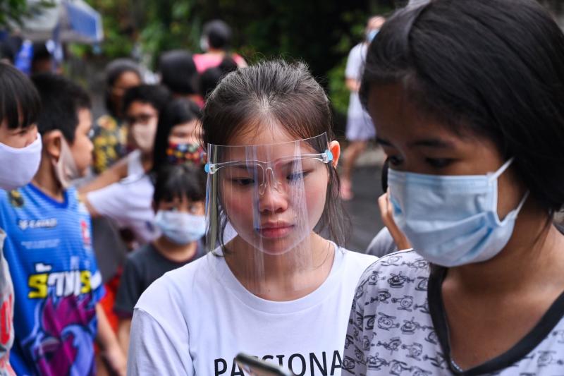 A girl wearing a plastic face shield joins people lining up for food and cash donations from Red Path Party, a political organisation, in Bangkok on Saturday, as Thai citizens are affected by the restrictive measure related to the Covid-19 novel coronavirus. (AFP photo)