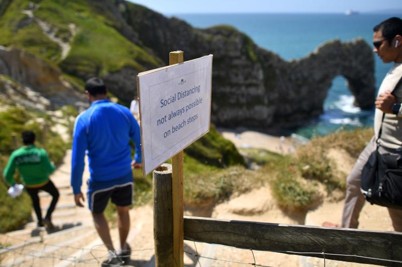 People pass a sign advising that social distancing may not be possible as they walk down a footpath towards the popular tourist spot Durdle Door near West Lulworth on the south coast of England on Sunday. (AFP photo) People pass a sign advising that social distancing may not be possible as they walk down a footpath towards the popular tourist spot Durdle Door near West Lulworth on the south coast of England on Sunday. (AFP photo)