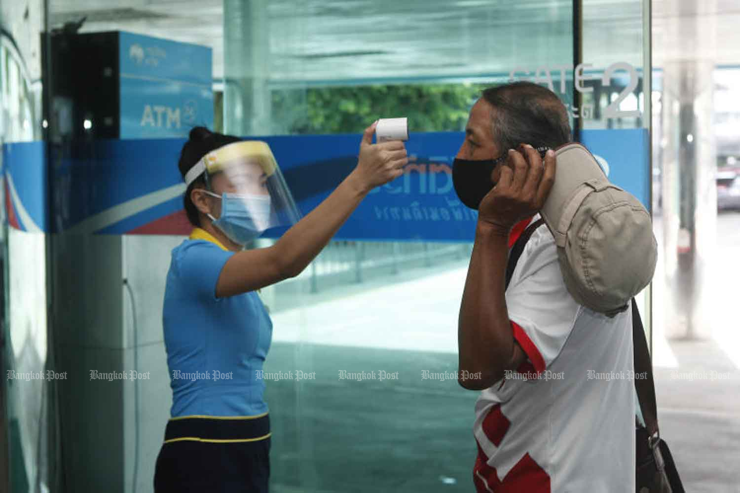 An inter-provincial bus employee checks the body temperature of a traveller at a private bus terminal in Chatuchak district of Bangkok on Friday. (Photo: Nutthawat Wicheanbut)