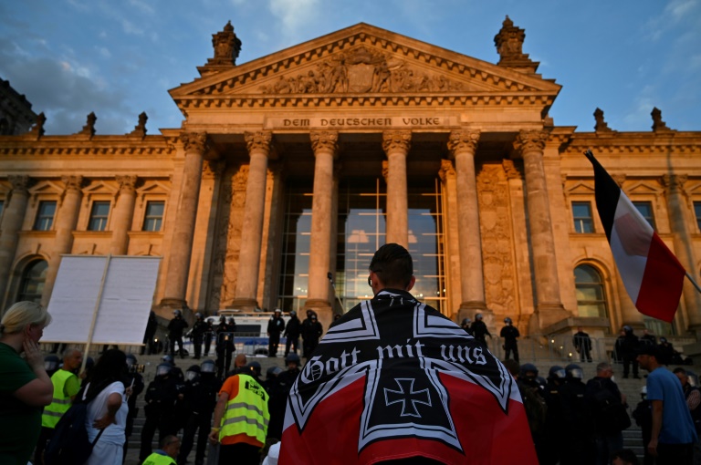 A protester wrapped in black-white-red imperial German flag stands in front of the Reichstag building in Berlin during a demonstration called by far-right and Covid-19 deniers to protest against restrictions related to the coronavirus pandemic. A protester wrapped in black-white-red imperial German flag stands in front of the Reichstag building in Berlin during a demonstration called by far-right and Covid-19 deniers to protest against restrictions related to the coronavirus pandemic.