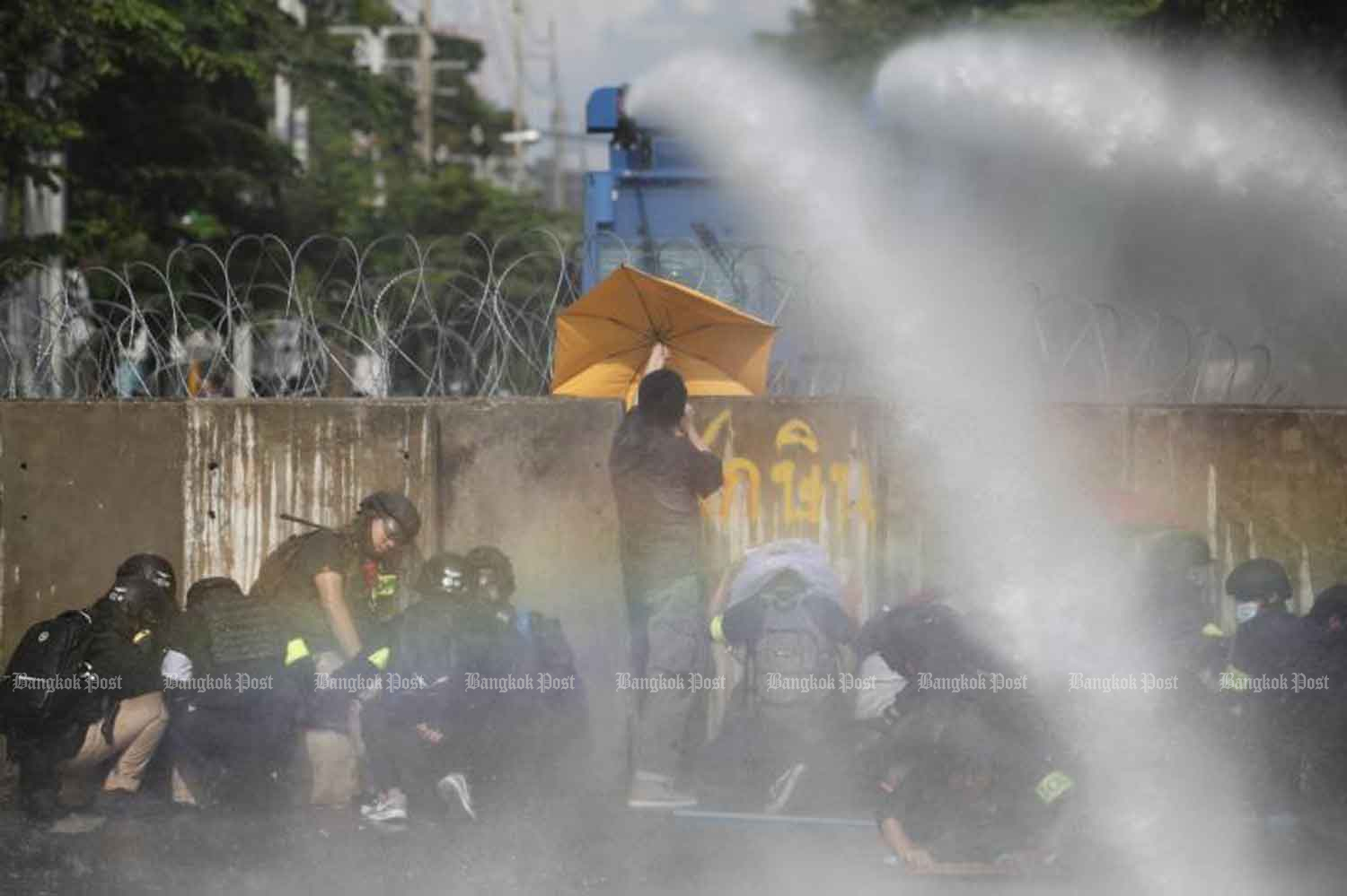 Demonstrators in protective gear take cover behind concrete barriers as riot police shoot water cannon to deter them from breaking through a barricade erected to block access to the parliament building, on Tuesday, in Dusit district of Bangkok. (Photo by Wichan Charoenkiatpakul)