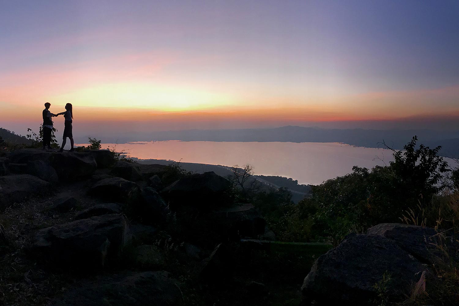 A couple stands on the top of Khao Yai Thiang hill. The place is known for its mountain bike trails during the day and also a place to observe beautiful sunsets and views of Lam Takhong reservoir.