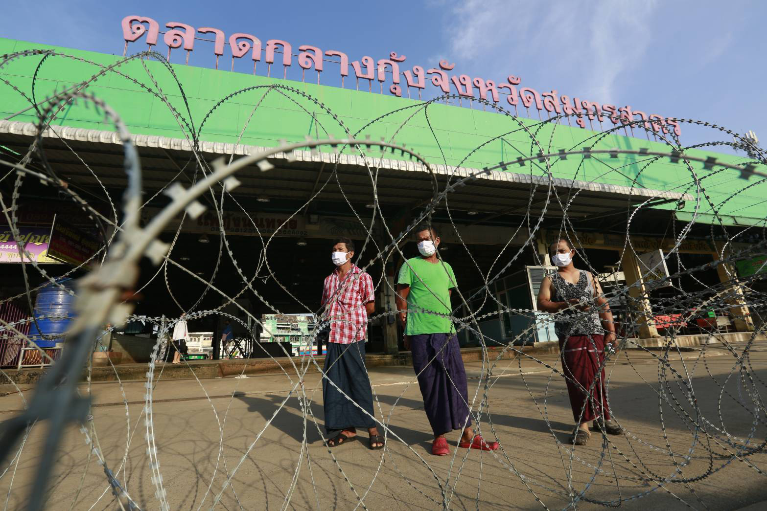 Migrant workers from Myanmar stand behind razor wire blocking the entrance to the Central Shrimp Market linked to an outbreak of Covid-19, in Muang district of Samut Sakhon on Sunday. (Photo by Arnun Chonmahatrakool)