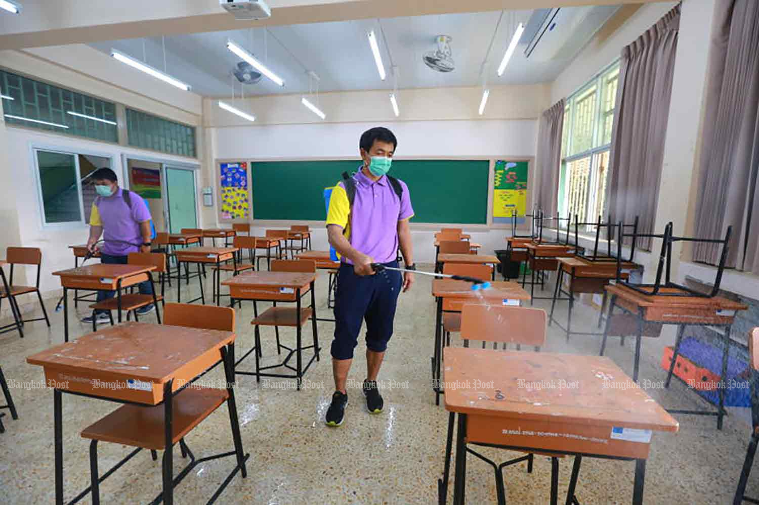 Teachers spray a disinfectant agent inside a classroom at Ban Bang Kapi School in Bangkok on Thursday ahead of the re-opening of 437 schools under the supervision of the Bangkok Metropolitan Administration next week. Photo by SOMCHAI POOMLARD