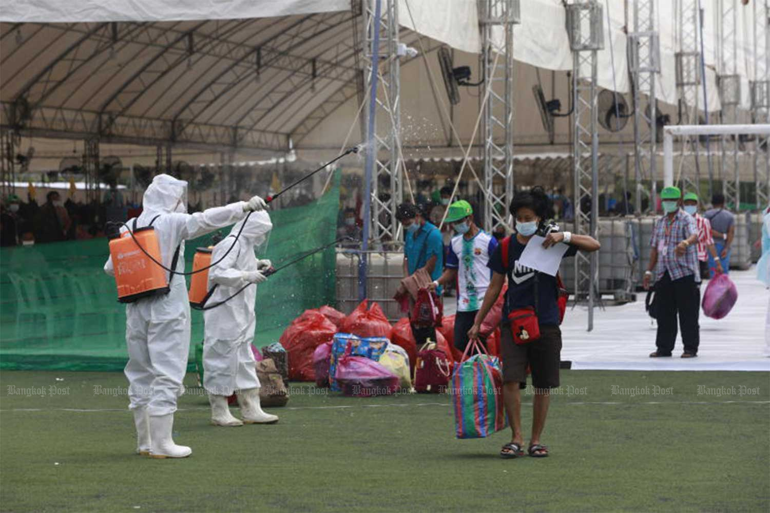 Migrant workers are sprayed with disinfectant as they leave the Covid-19 field hospital at Samut Sakhon’s provincial stadium, after completing their quarantine period on Jan 10. (File photo: Arnun Chonmahatrakoo)