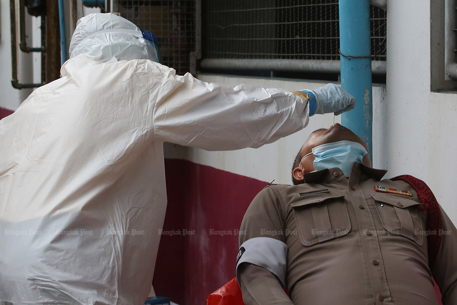Try not to sneeze: A medical worker wearing protective gear takes a swab sample for a Covid-19 test from a policeman attached to Min Buri police station. Two officers at the station have tested positive and 39 others are classifed as ‘high-risk’ and are under quarantine. (Photo by Pattarapong Chatpattarasil) Try not to sneeze: A medical worker wearing protective gear takes a swab sample for a Covid-19 test from a policeman attached to Min Buri police station. Two officers at the station have tested positive and 39 others are classifed as ‘high-risk’ and are under quarantine. (Photo by Pattarapong Chatpattarasil)