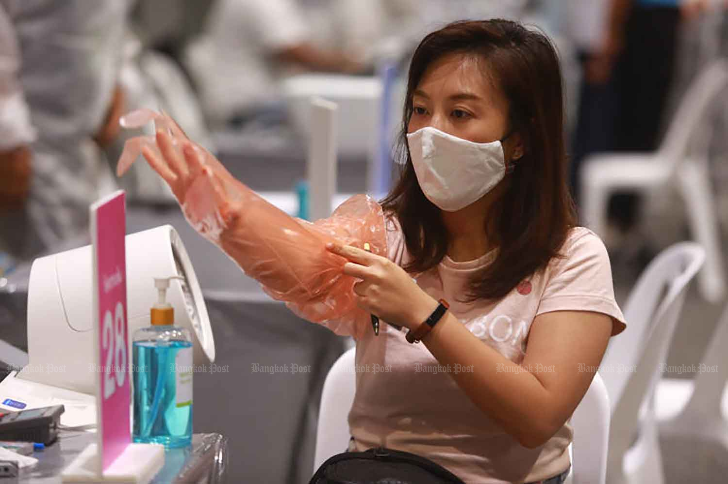 A woman puts on a long glove before having her blood pressure taken on Thursday ahead of her Covid-19 vaccine at Samyan Mitrtown shopping mall in Bangkok's Pathumwan district. (Photo: Somchai Poomlard) A woman puts on a long glove before having her blood pressure taken on Thursday ahead of her Covid-19 vaccine at Samyan Mitrtown shopping mall in Bangkok's Pathumwan district. (Photo: Somchai Poomlard)