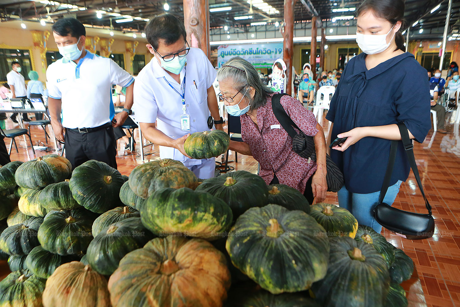 A medical worker selects a pumpkin for a woman after she received a Covid-19 vaccination at Wat Bang Phli Klang in Samut Prakan. The temple abbot has given away free pumpkins to encourage people to have their jabs. (Photo by Somchai Poomlard) A medical worker selects a pumpkin for a woman after she received a Covid-19 vaccination at Wat Bang Phli Klang in Samut Prakan. The temple abbot has given away free pumpkins to encourage people to have their jabs. (Photo by Somchai Poomlard)