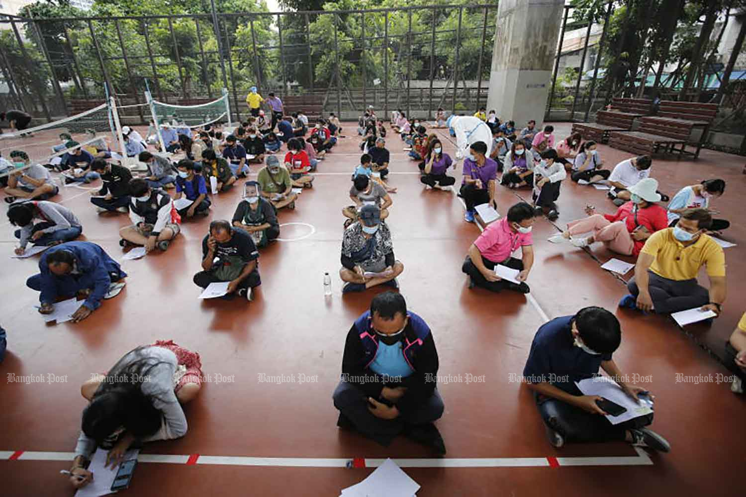 People sit apart on the floor as nurses examine their medical forms before a Covid-19 test at the PAT sporting ground in Ratchathewi district, Bangkok, on Tuesday. (Photo: Wichan Charoenkiatpakul)