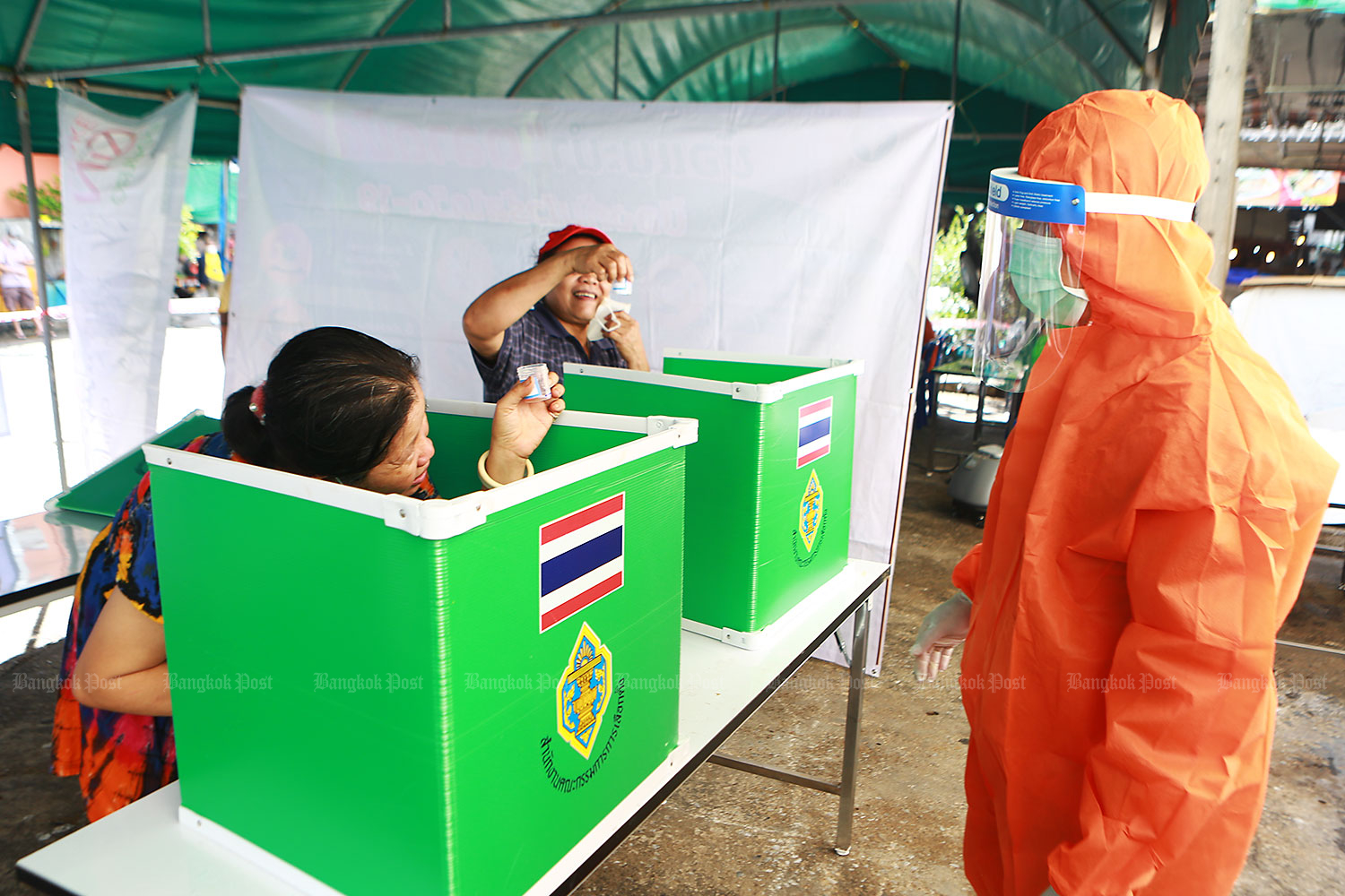 Will this do?: Women hold up saliva samples at improvised cubicles as a medical worker in full protective gear waits to collect them. The samples were for Covid-19 testing on people in at-risk groups in Yannawa district. (Photo: Somchai Poomlard) Will this do?: Women hold up saliva samples at improvised cubicles as a medical worker in full protective gear waits to collect them. The samples were for Covid-19 testing on people in at-risk groups in Yannawa district. (Photo: Somchai Poomlard)