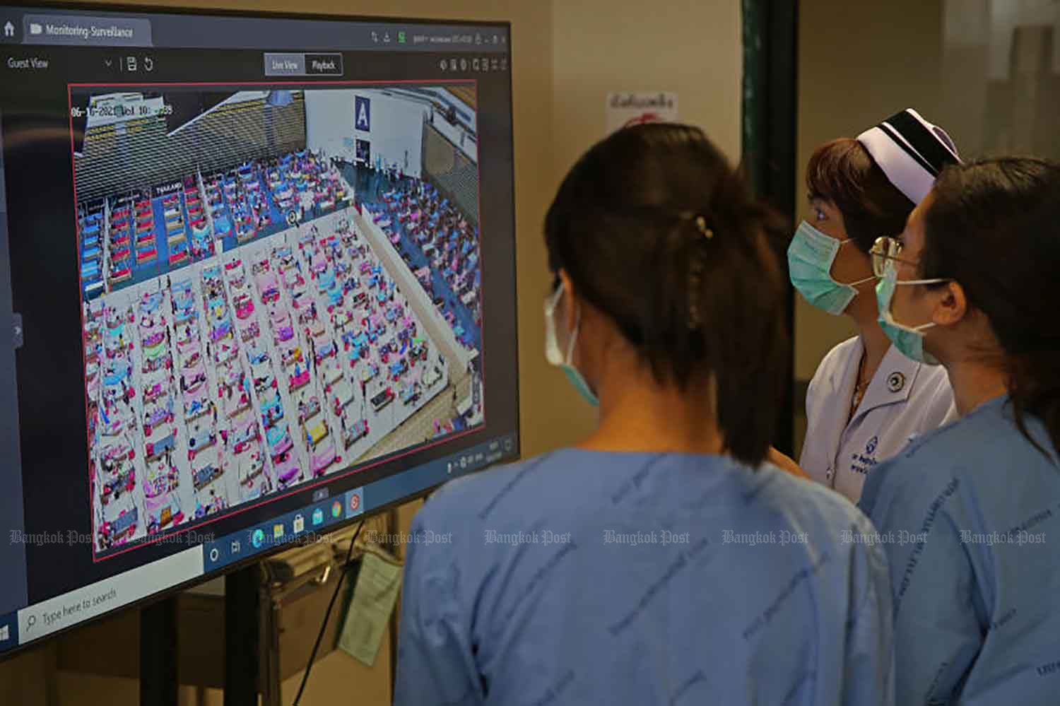 Nurses monitor Covid-19 patients through a closed-circuit camera at the Erawan 2 field hospital at Bangkok Arena on Wednesday. The facility cares for patients with mild and moderate symptoms and is supervised by medical staff around the clock. (Photo: Varuth Hirunyatheb)