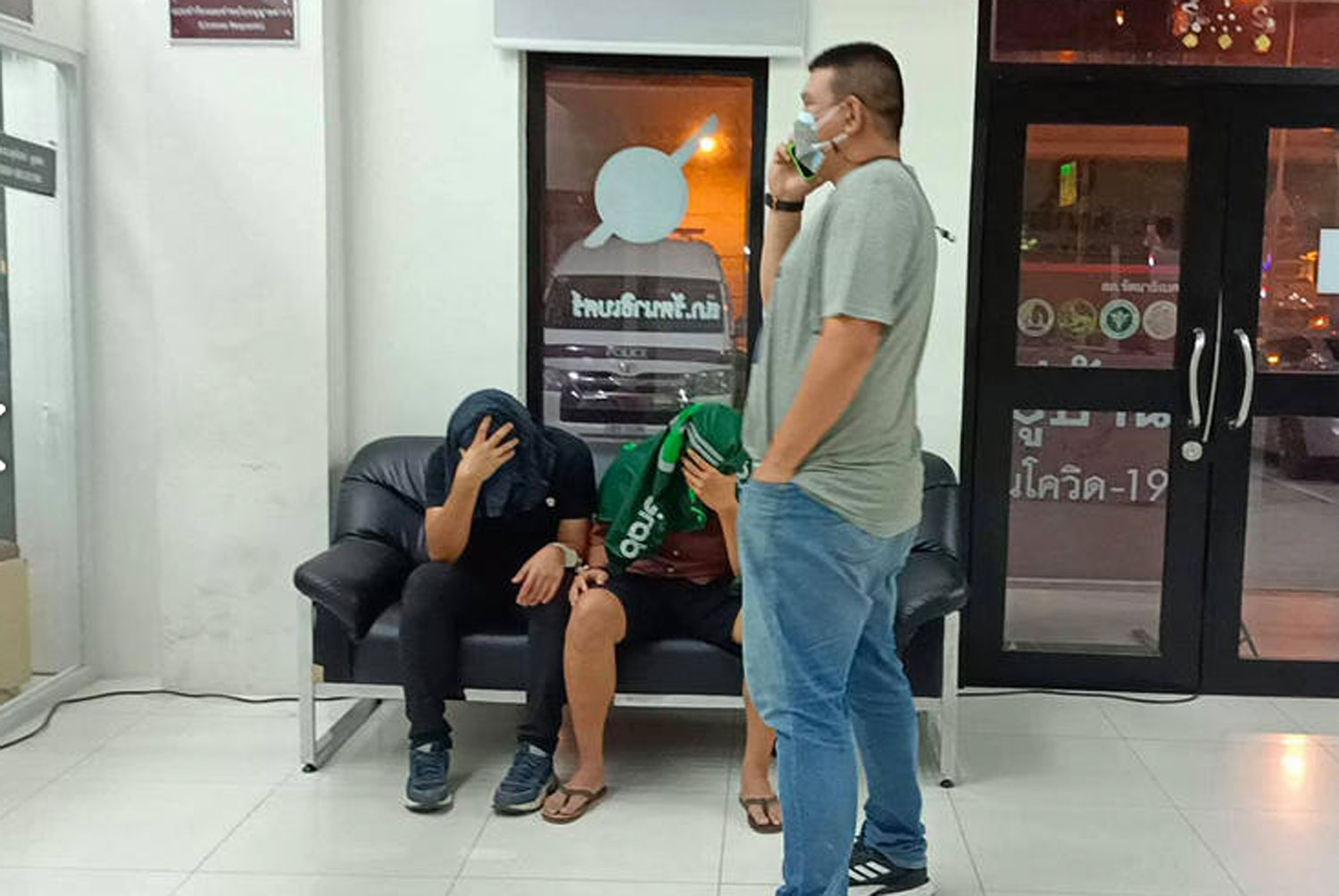 The two suspects, Cpl Vorasart Lailang, 31, of Khon Kaen and Nawatkorn Pongassaphon, 31, of Nakhon Ratchasima (both seated), cover their faces at Rattanathibet police station after their arrest on Wednesday night for extortion. (Photo: FM91bkk.com)