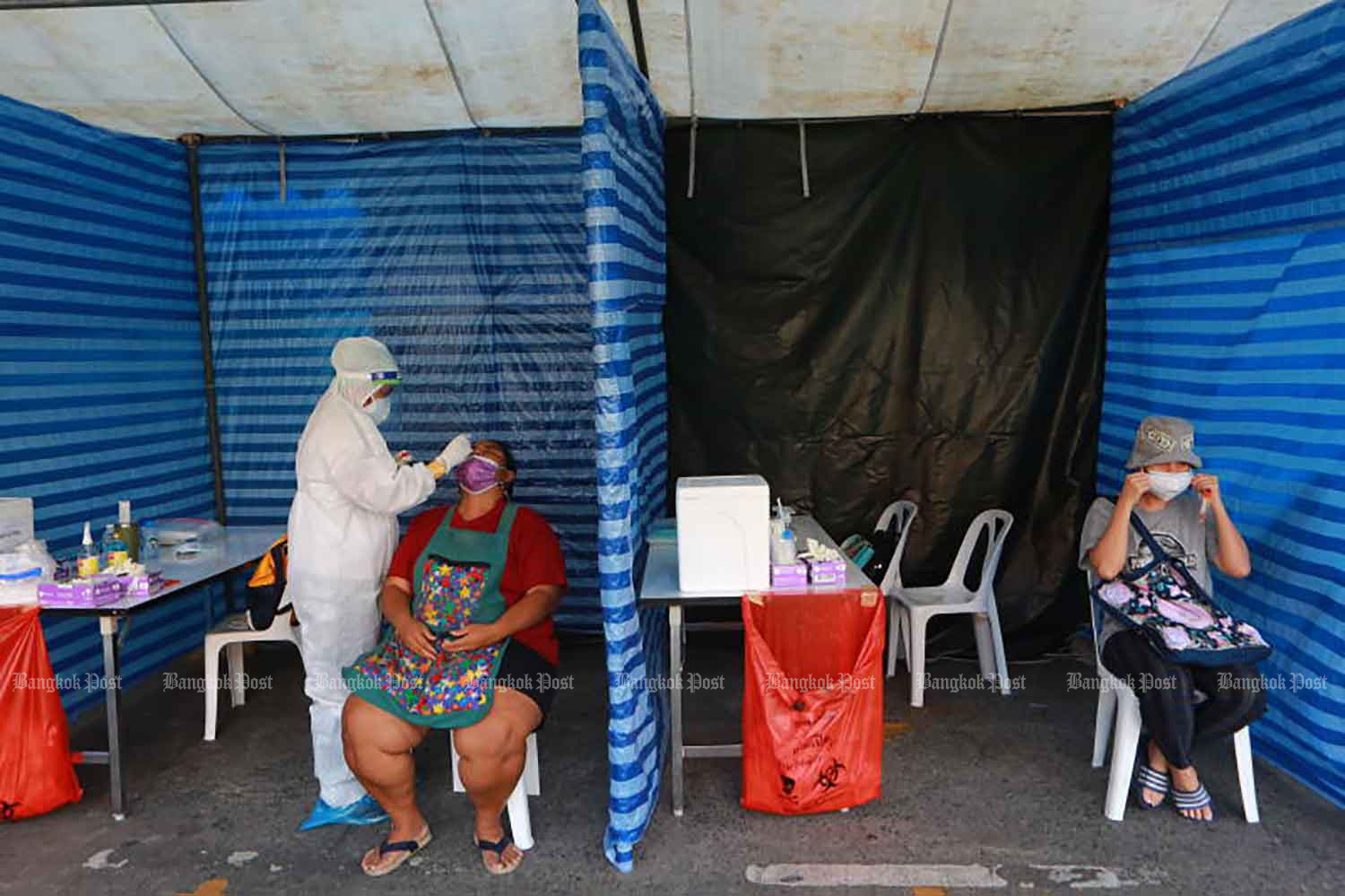 Covid-19 tests being administered at a makeshift site outside Bo Be Tower on Damrongrak Road in Bangkok's Pomprap Sattruphai district on Tuesday. The mobile unit is part of proactive screening in the district where clusters of infections among migrant workers have been reported. (Photo: Somchai Poomlard)