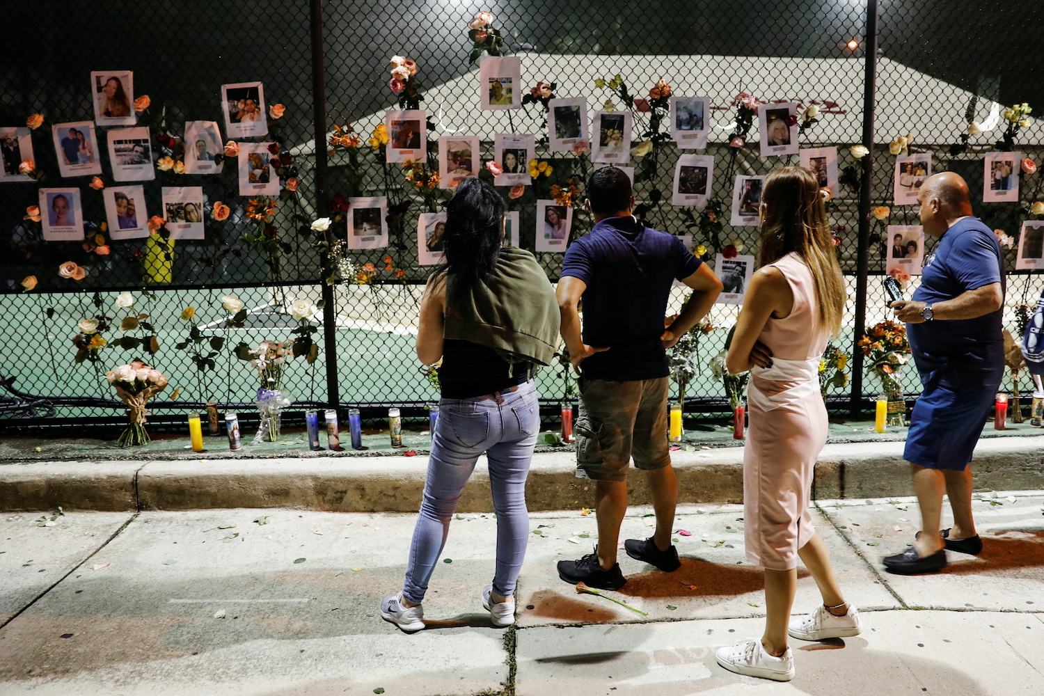 People look at flowers and pictures of missing people hanging on a fence at a memorial for victims of a partially collapsed condominium building in Surfside, near Miami Beach, Florida, on Friday evening. (Reuters Photo) People look at flowers and pictures of missing people hanging on a fence at a memorial for victims of a partially collapsed condominium building in Surfside, near Miami Beach, Florida, on Friday evening. (Reuters Photo)