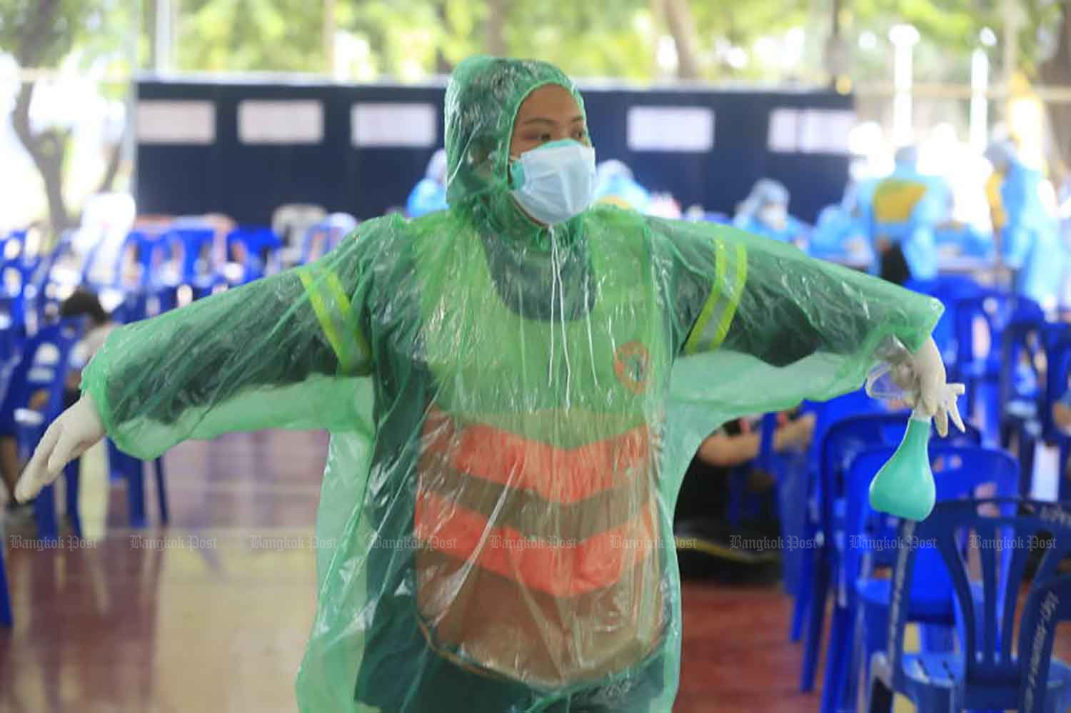 A City Hall worker shows off her improvised protective gear made from a plastic raincoat, as officials from Chatuchak district office assist people arriving for  Covid-19 testing at the sports ground at Chadrakasem Rajabhat University in the capital on Monday. (Photo: Pornprom Satrabhaya)