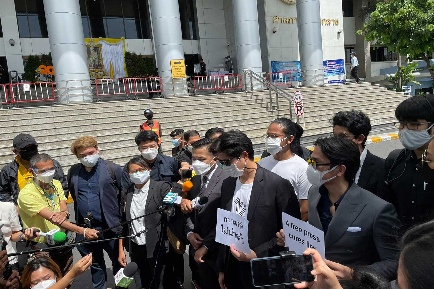 Media representatives and human rights lawyers talk to reporters before filing a lawsuit at the Civil Court against a prime minister's order they say threatens press freedom and free speech. A message on the paper signs they hold reads "a free press cures lies." (Photo: @HRLawyersTH Twitter account)