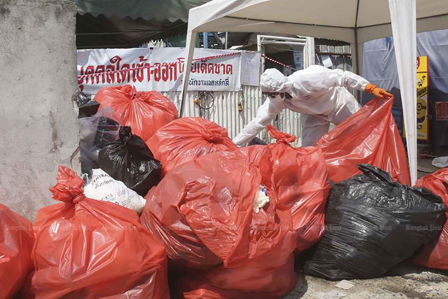 A worker in a protective suit sorts garbage outside a dormitory at a construction site near the government complex on Chaeng Watthana Road, where a new cluster of Covid-19 infections has been detected in May. (Photo: Pattarapong Chatpattarasill)